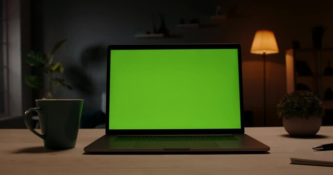 Modern laptop with template copy space green screen set on table in living room at home at night for distant learning or remote work green screen template 4k close up
