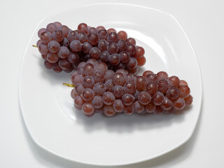 Grapes (Delaware) on a plate. The grapes have water droplets on their surface. White background.