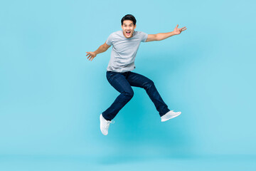 Fototapeta na wymiar Energetic happy young Asian man in casual clothes jumping studio shot isolated in light blue background