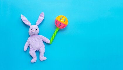 Rabbit toy with colorful baby rattle on blue background.