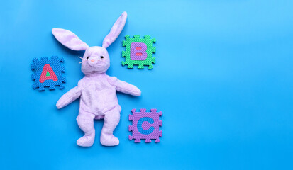 Rabbit toy with english alphabet puzzle on blue background. Education concept