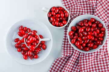 Cornel berries in different plates on a white and picnic cloth background. flat lay.