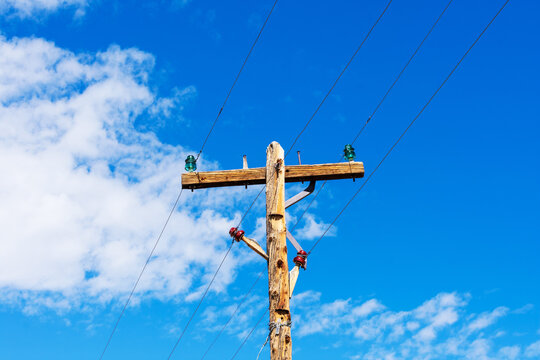 Weathered wooden utility pole with parallel single-circuit lines and colorful isolators in the blue sky