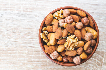 a mixture of nuts in a clay plate on a wooden table, a concept of healthy food, top view