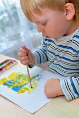 Child of three years old draws with paints on sheet of paper. Vertical shot