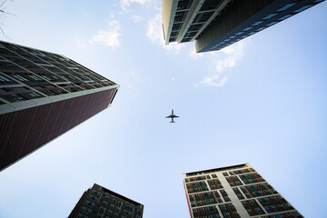 Fototapeta na wymiar Airplane flying through the sky seen through buildings