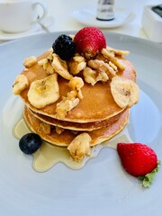 White plate full of pancakes with strawberries raspberries blueberries and honey