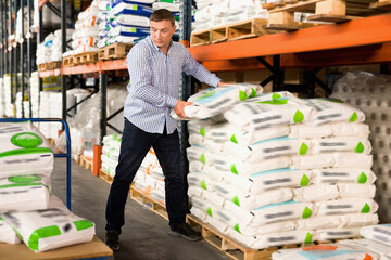Glad smiling Man choosing compost soil in plastic bags in hypermarket .