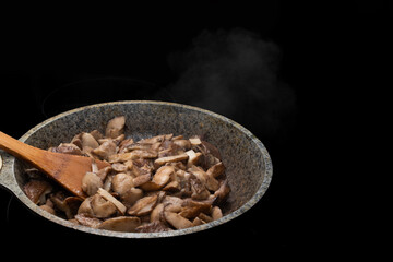 Close-up of a wooden spoon and fried or stewed mushrooms in a skillet, steam rises from hot mushrooms