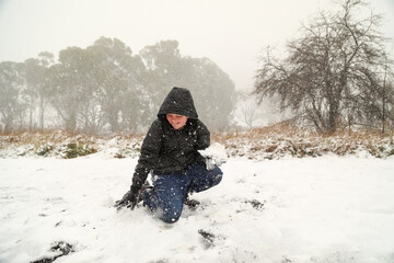 Fototapeta na wymiar Boy playing in fresh snow making snow balls during snow storm in New South Wales, Australia