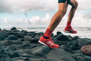 Running shoes of athlete man jogging on beach. Difficult terrain with wet rocks for training...