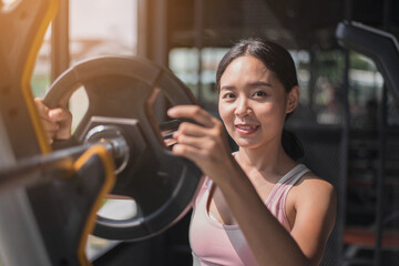 Fit young woman in sportswear working out at the gym. fit asian woman putting more weight splate on barbell