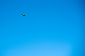 A small green plane flies against a bright blue cloudless sky.