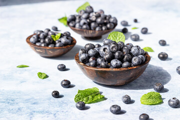 Freshly picked juicy blueberries in wooden bowl with mint on blue background. Antioxidant. Concept for healthy eating and nutrition. Bright light and trendy shadows.