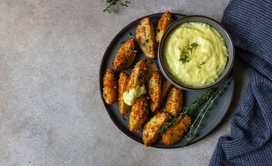 Baked crispy potato wedges with cheese sauce and thyme on ceramic plate. Homemade snack food.