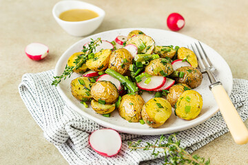 Tasty hot potato salad with green beans, fresh radishes and herbs dressing with olive oil and mustard sauce, light background.