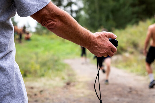 Close-up of a trainer holding a stopwatch in his hand and measuring the speed of short-distance running of athletes, in the background beautiful nature