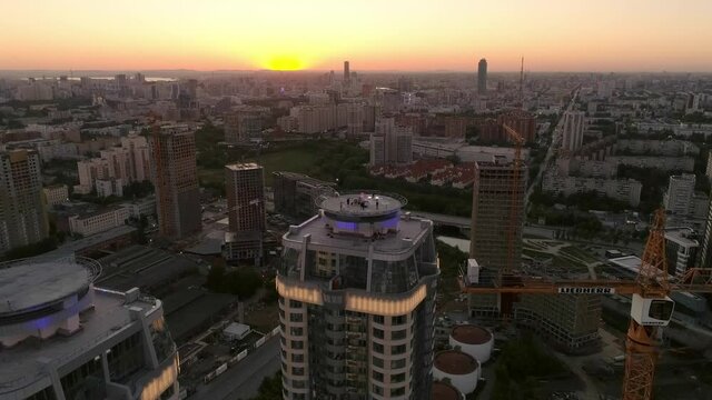 Aerial view of Party on the roof of a skyscraper. Evening summer warm city at sunset. Near construction site, buildings and tower cranes
