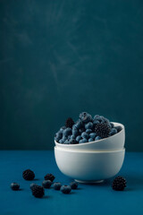Fototapeta na wymiar White bowl with mix blueberry and blackberry on blue background.