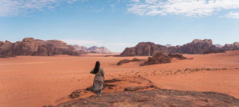 Young Asian traveller with local Arab dress standing on top of mountain and enjoying landscape of Wadi Rum desert, Jordan, Arab. Panoramic banner portion