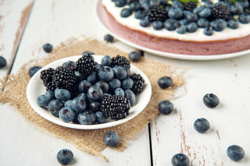 Plate with blackberry and blueberry on the burlap napkin and cottage cheese casserole on background.
