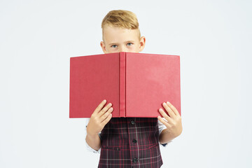 The schoolboy holds books, hiding his face behind them. Isolated background.