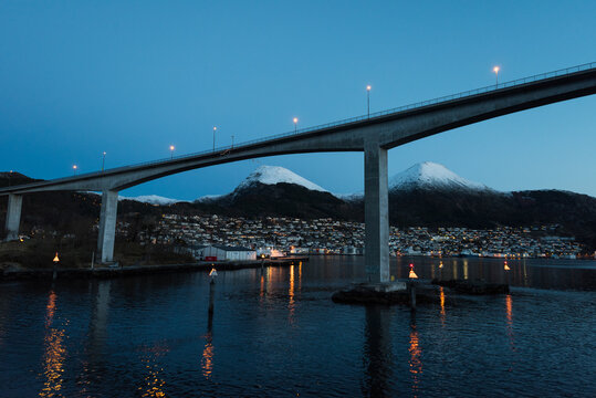Bridge over fjord near the city Maloy in Norway seen from cruise ship in early morning with snow capped mountains on clear winter day