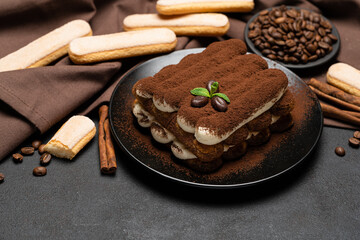 Classic tiramisu dessert on ceramic plate and savoiardi cookies on concrete background