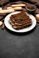Classic tiramisu dessert on ceramic plate and savoiardi cookies on concrete background