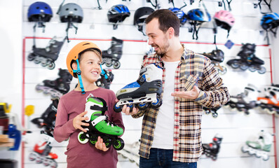 Adult father and boy boasting purchased roller-skates in sports store