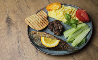 Fried fish, meat steak and vegetables on a plate. On a wooden table