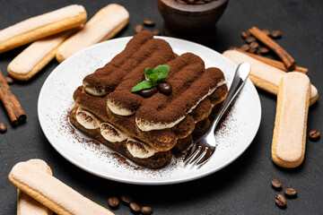 Classic tiramisu dessert on ceramic plate and savoiardi cookies on concrete background