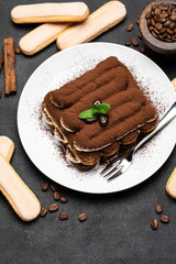 Classic tiramisu dessert on ceramic plate and savoiardi cookies on concrete background