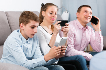 Middle-aged happy family playing with their smartphones together at home