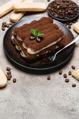Classic tiramisu dessert on ceramic plate and savoiardi cookies on concrete background