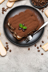 Classic tiramisu dessert on ceramic plate and savoiardi cookies on concrete background