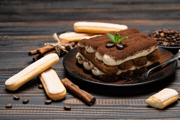 Classic tiramisu dessert on ceramic plate and savoiardi cookies on wooden background