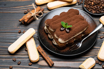 Classic tiramisu dessert on ceramic plate and savoiardi cookies on wooden background