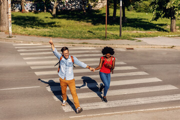 Young cheerful couple running over street and smiling.