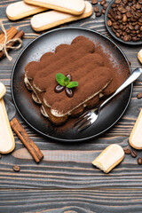 Classic tiramisu dessert on ceramic plate and savoiardi cookies on wooden background