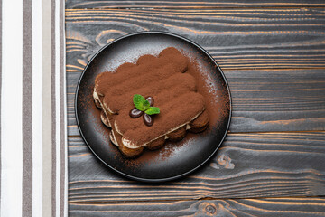 Classic tiramisu dessert on ceramic plate on wooden background