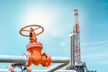 Fountain fittings of a gas well with high-pressure gate valve handwheels. Oil and Gas drilling rig is in the background. Top drive system of drilling rig