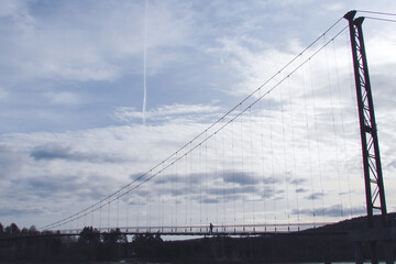 Side view of the pedestrian suspension bridge over the river. Contour light.