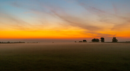 Naklejka na ściany i meble Colorful warm sunset over rural field covered with fog and mist, in autumn