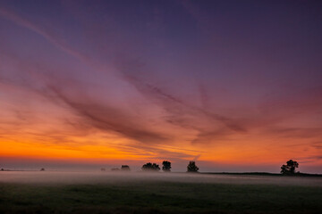 Colorful warm sunset over rural field covered with fog and mist, in autumn