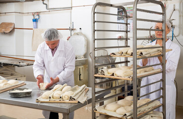 Experienced baker working with female assistant in bakery, forming bread loaves from raw dough