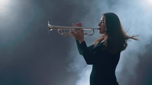 Young woman in smoky studio plays on piccolo trumpet