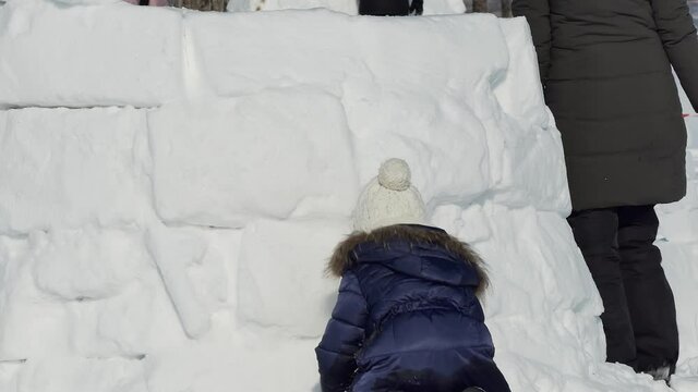 Igloo. The girl covers the seams with snow between the snow blocks. Participants and spectators build a Igloo out of snow. Novosibirsk, Russia / Siberia, February / 15 / 2020, annual holiday "Eskimo c
