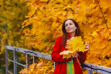 Naklejka na ściany i meble Portrait of pretty young woman of Slavic appearance in yellow colored dress and red coat in autumn, walk in forest. Cute model walks in Park in golden autumn against background of nature