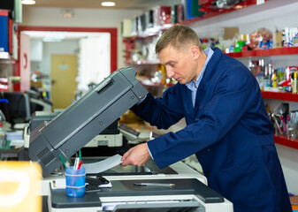 Portrait of confident service engineer standing by photocopy machine in office. High quality photo